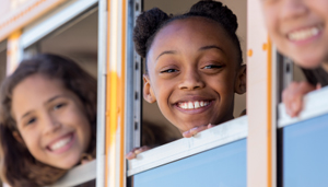 Middle school students smiling with their faces in open school bus windows