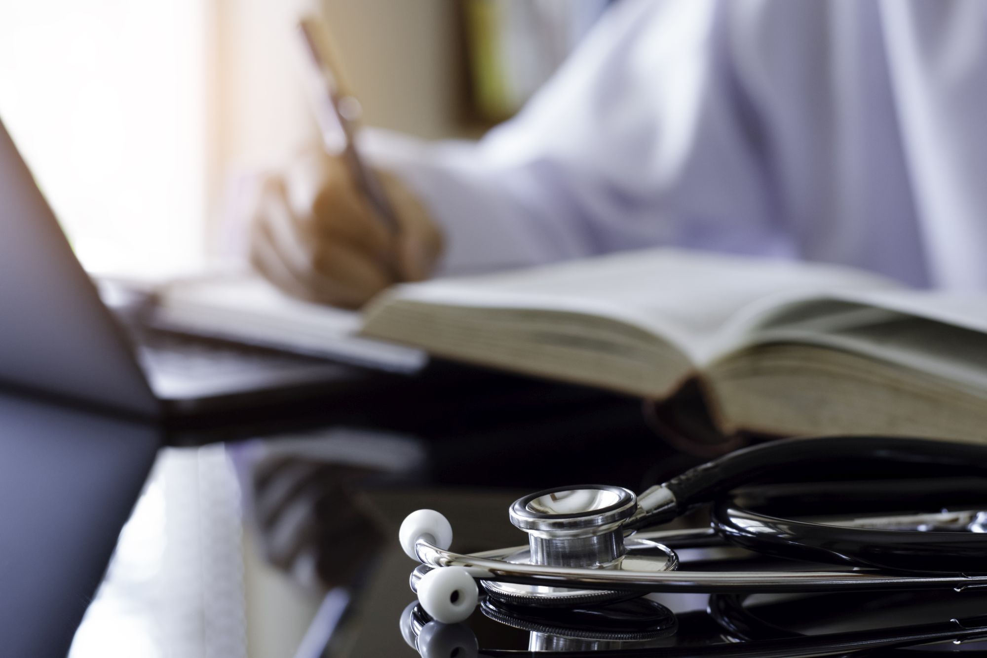 A stethoscope in the foreground with someone writing in the background