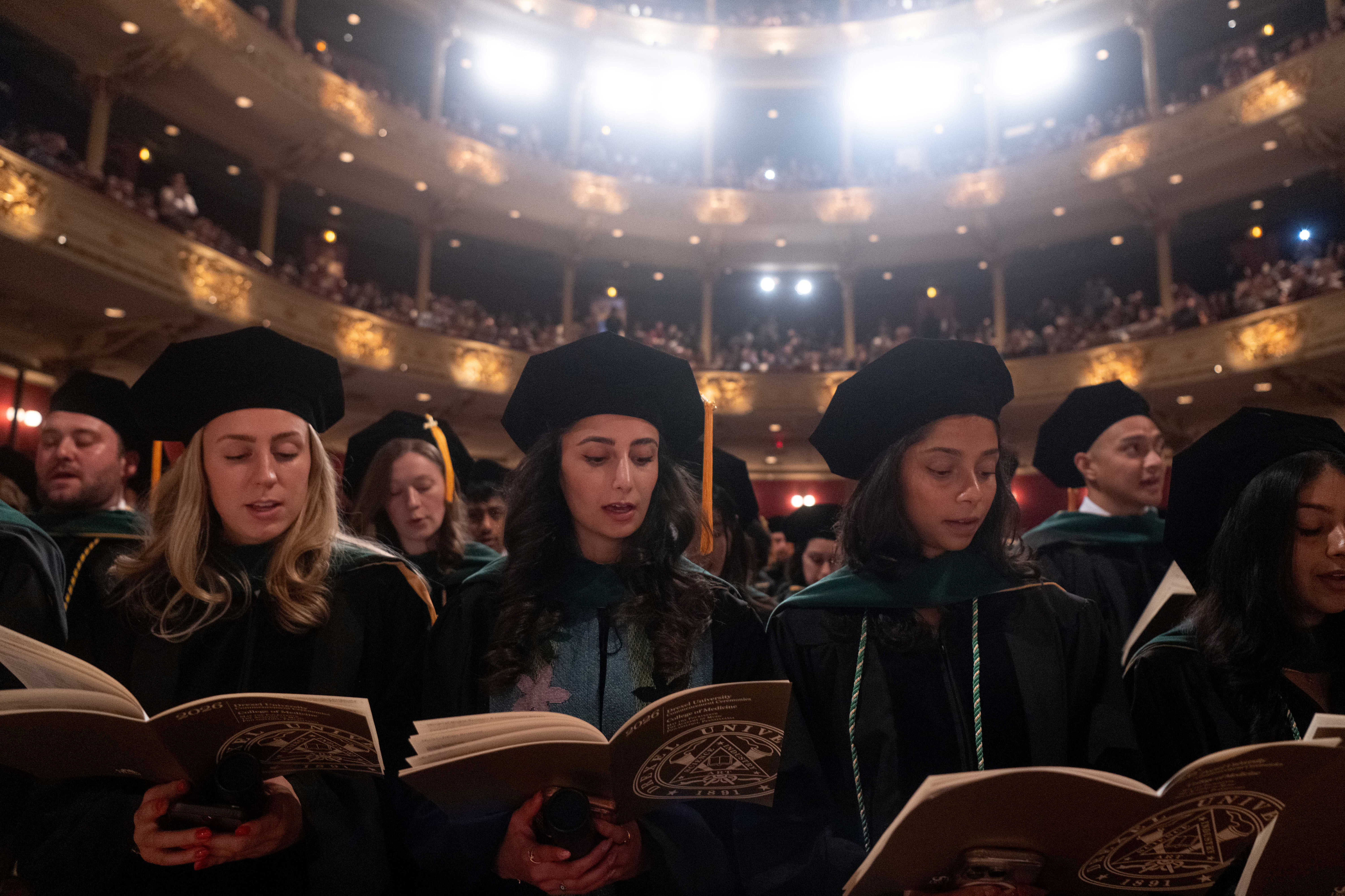 group of graduates saying oath while looking down at booklet