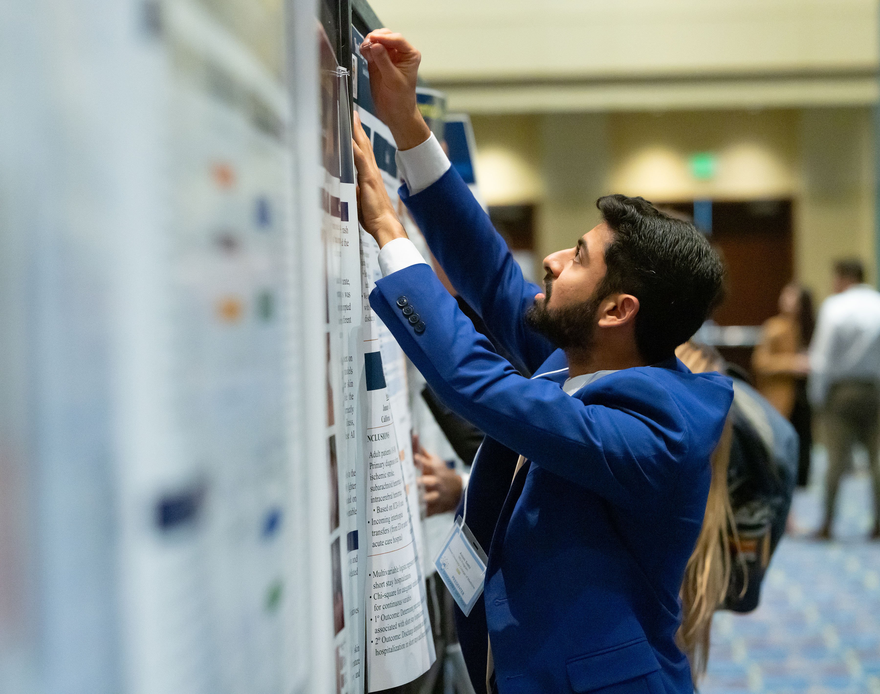 student tacks poster to wall between other posters