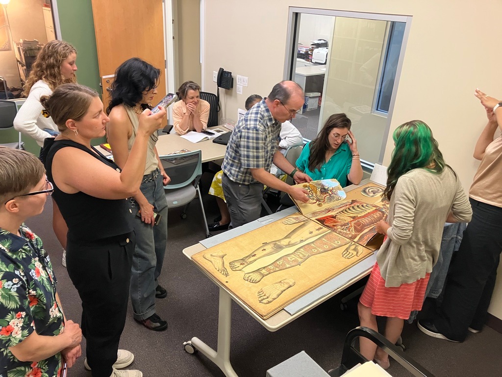 Members of The Woman Question creative team looking at a large 'flip-book' anatomy book
