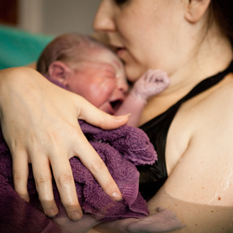 Mother holding newborn in birthing tub after home water birth.