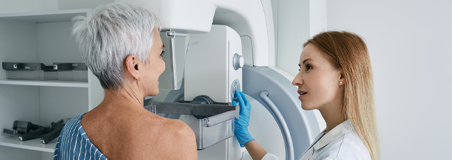 Senior woman having mammography scan at hospital with medical technician.