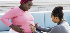 Pregnant woman with doula touching baby bump.