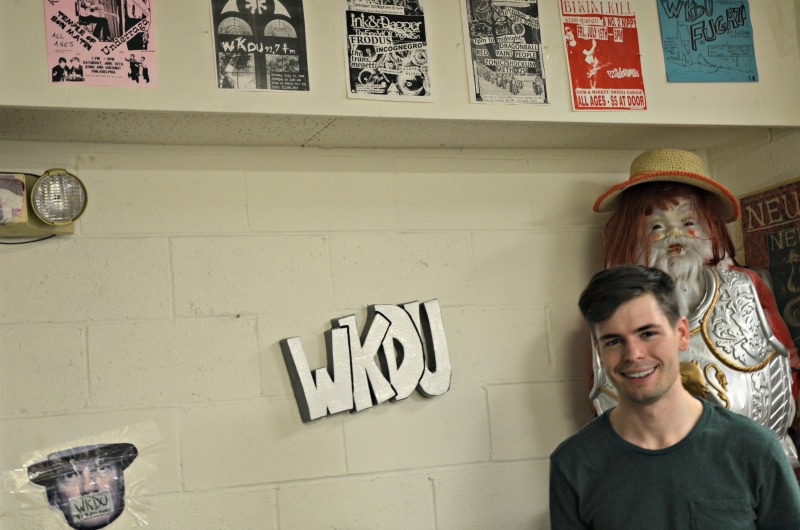 Senior communications major and WKDU DJ Nick Stropko stands in front of old WKDU concert posters in the college radio station's studio.