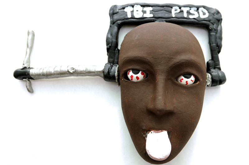 Another masks created by a participant in the art therapy program. This mask featured a vice tightened on the head that bears the abbreviations for traumatic brain injury and post-traumatic stress disorder.