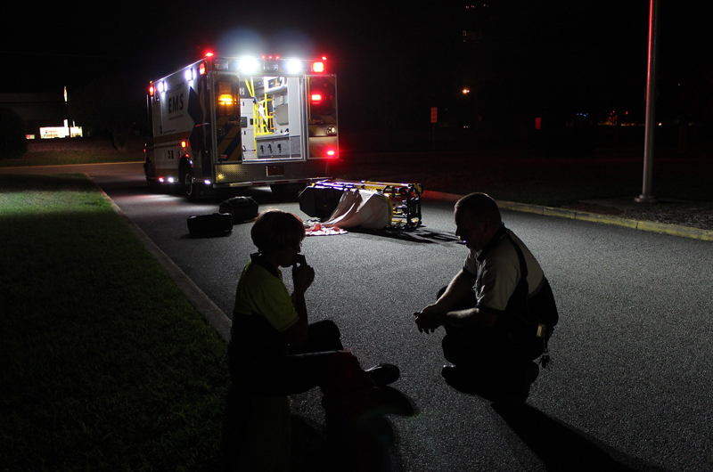 An EMT crouching in the dark with a patient outside an ambulance