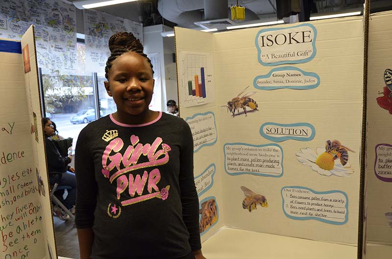 Sanaa Ward, a fourth-grade student at Belmont Charter, stands in front of the poster she helped create.