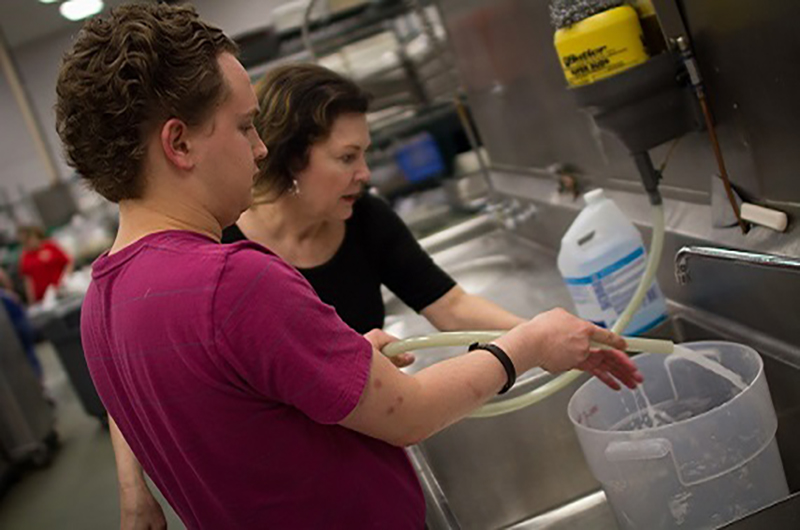 Woman helping young man fill bucket at sink 