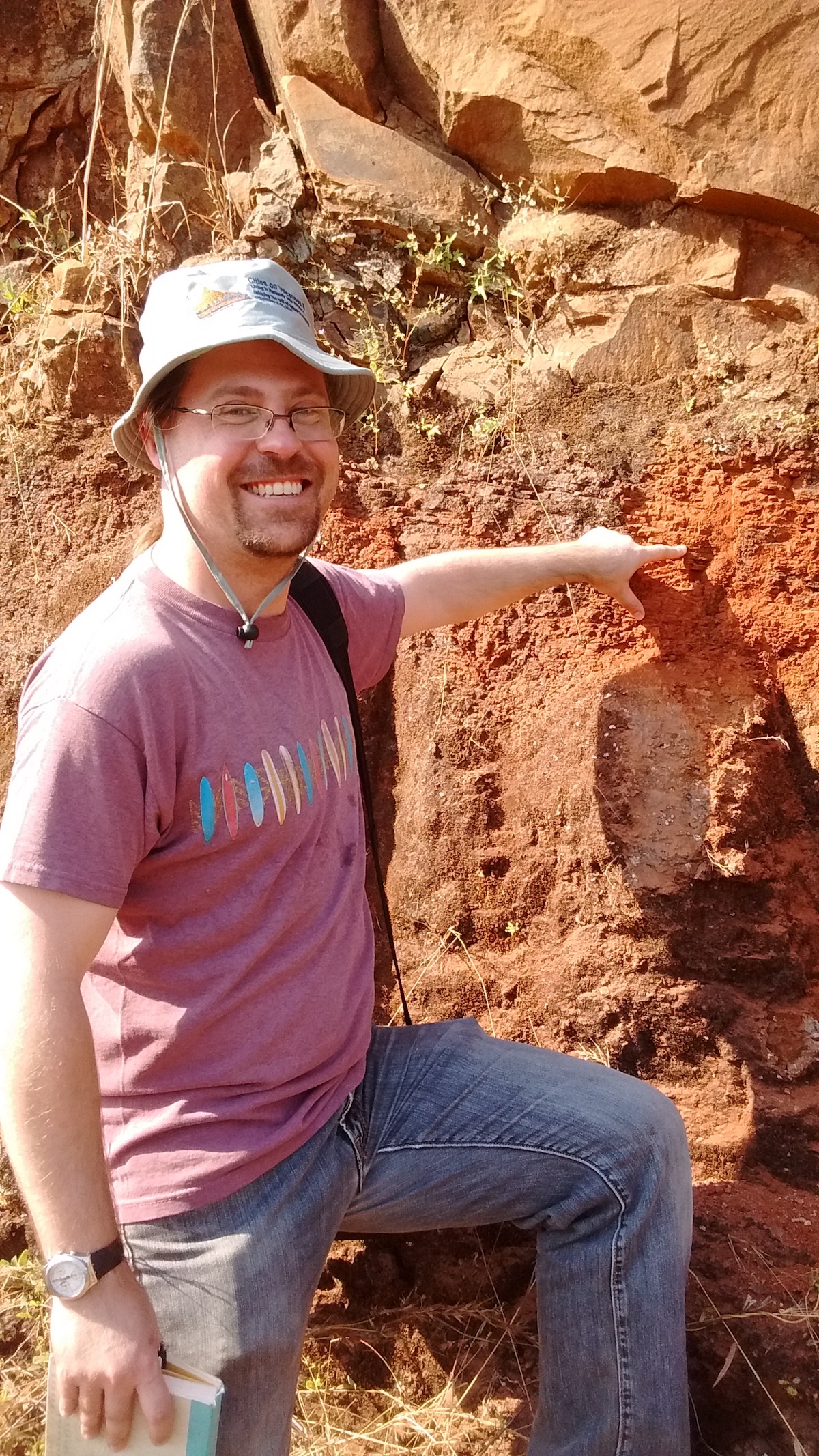 Vanderkluysen points at a red bole that marks the Bushe-Poladpur contact/Cretaceous-Paleogene boundary near the town of Poladpur in the Western Ghats. Image credit, Courtney Sprain.