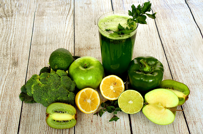 Green fruits and vegetables surrounding a glass containing a green smoothie.