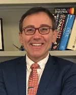 Headshot of Rogelio Miñana smiling in glasses and suit in front of bookcase.