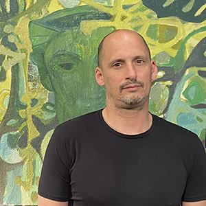 Image of Josh Weiss looking at camera in black t shirt in front of green and yellow painting