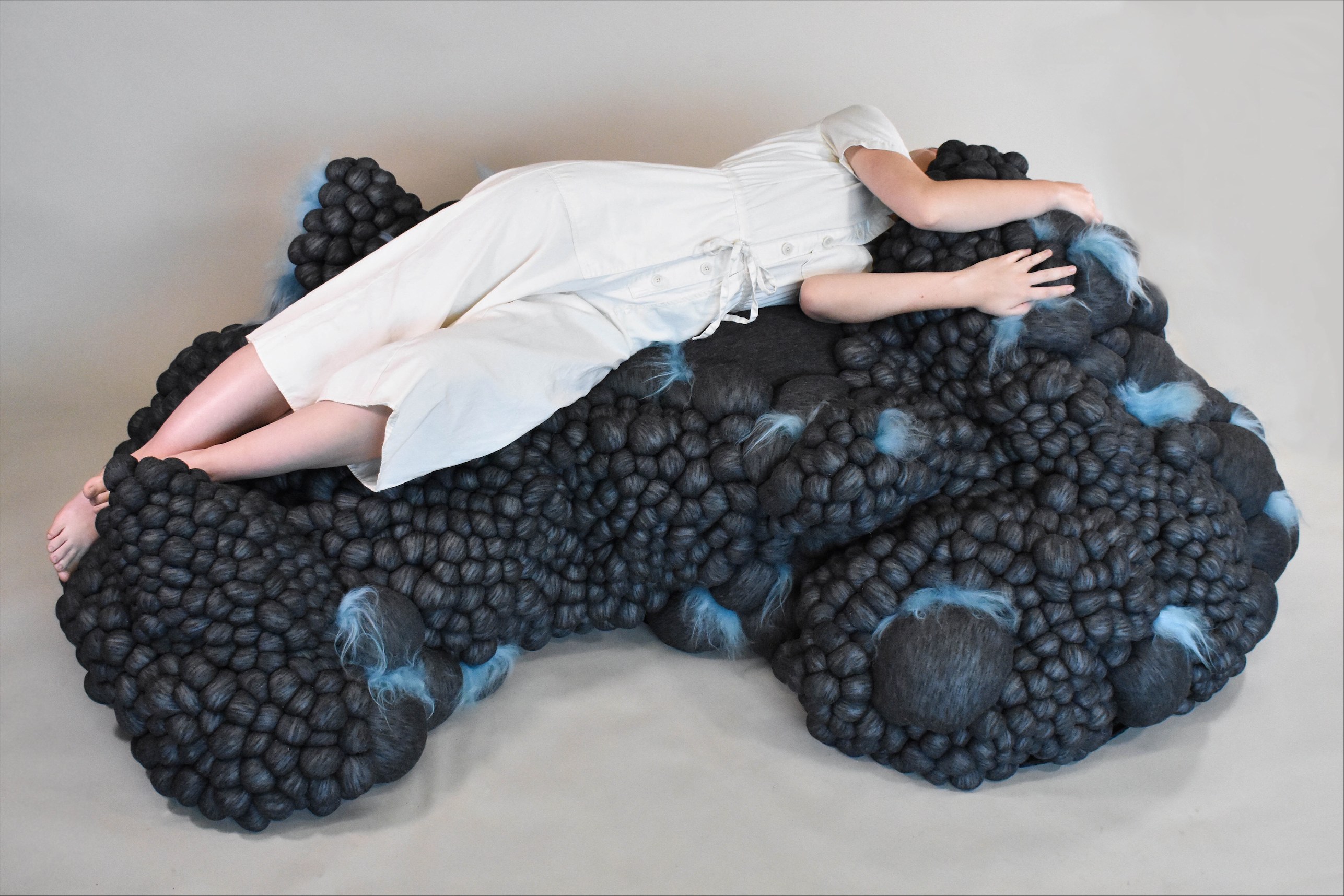 A person reclines on an organic-looking seating system composed of black nodules and tufts of blue fur