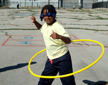 Photograph of young girl hula hooping on cracked asphalt in playground
